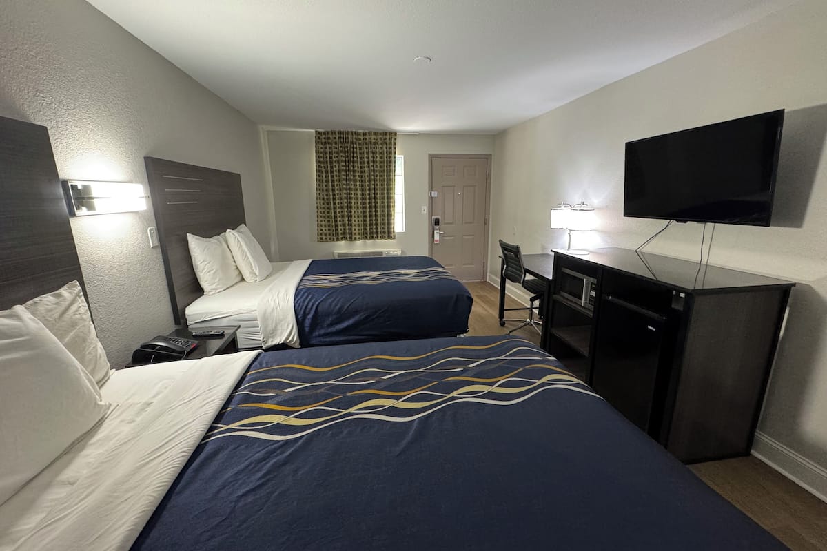 A hotel room with two beds, a desk, a television, and a window with curtains.