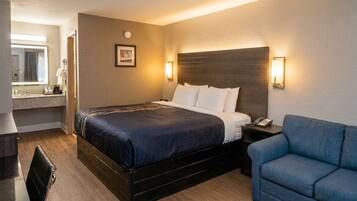 A hotel room with a bed, bedside table, lamp, and a blue armchair.