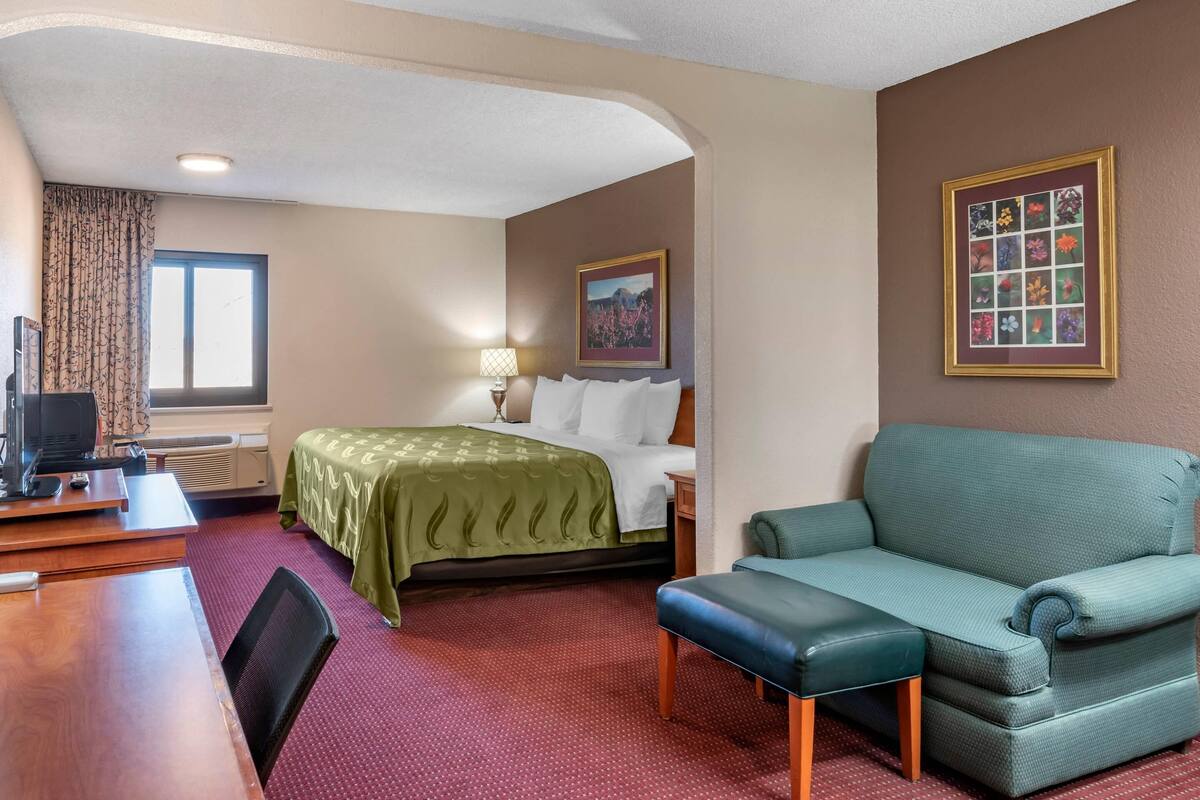 A hotel room with a bed, a green sofa, a desk, and a TV.