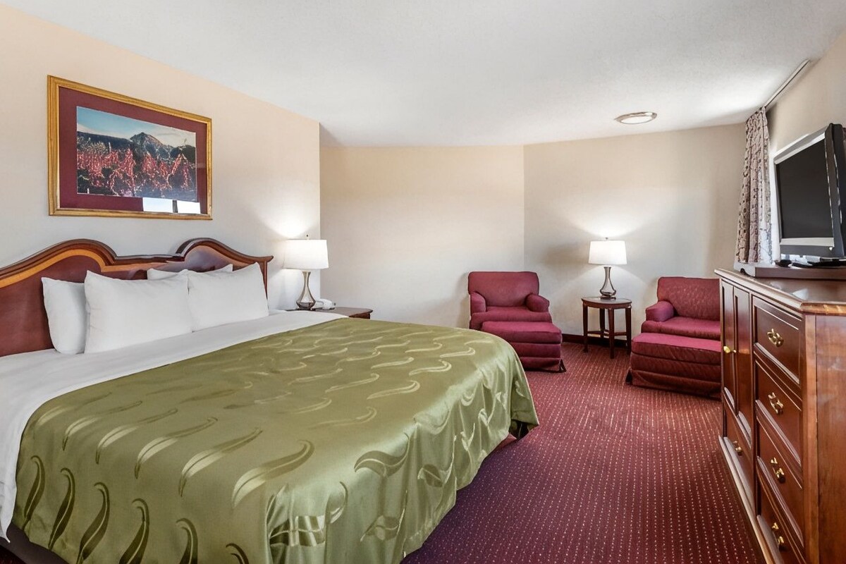 A hotel room with a bed, two armchairs, a TV, and a dresser.