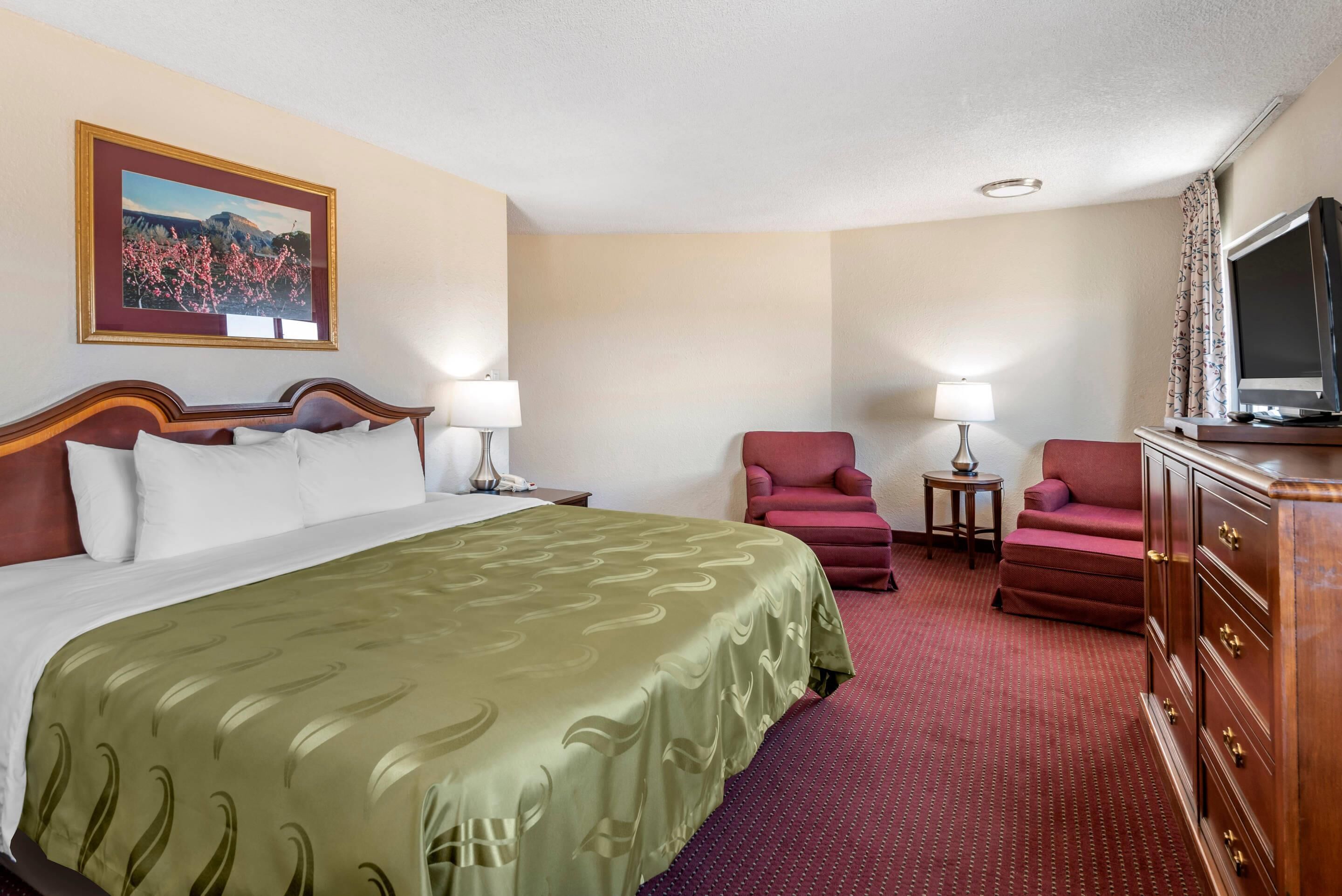 A hotel room with a large bed, two armchairs, a TV, and a dresser.