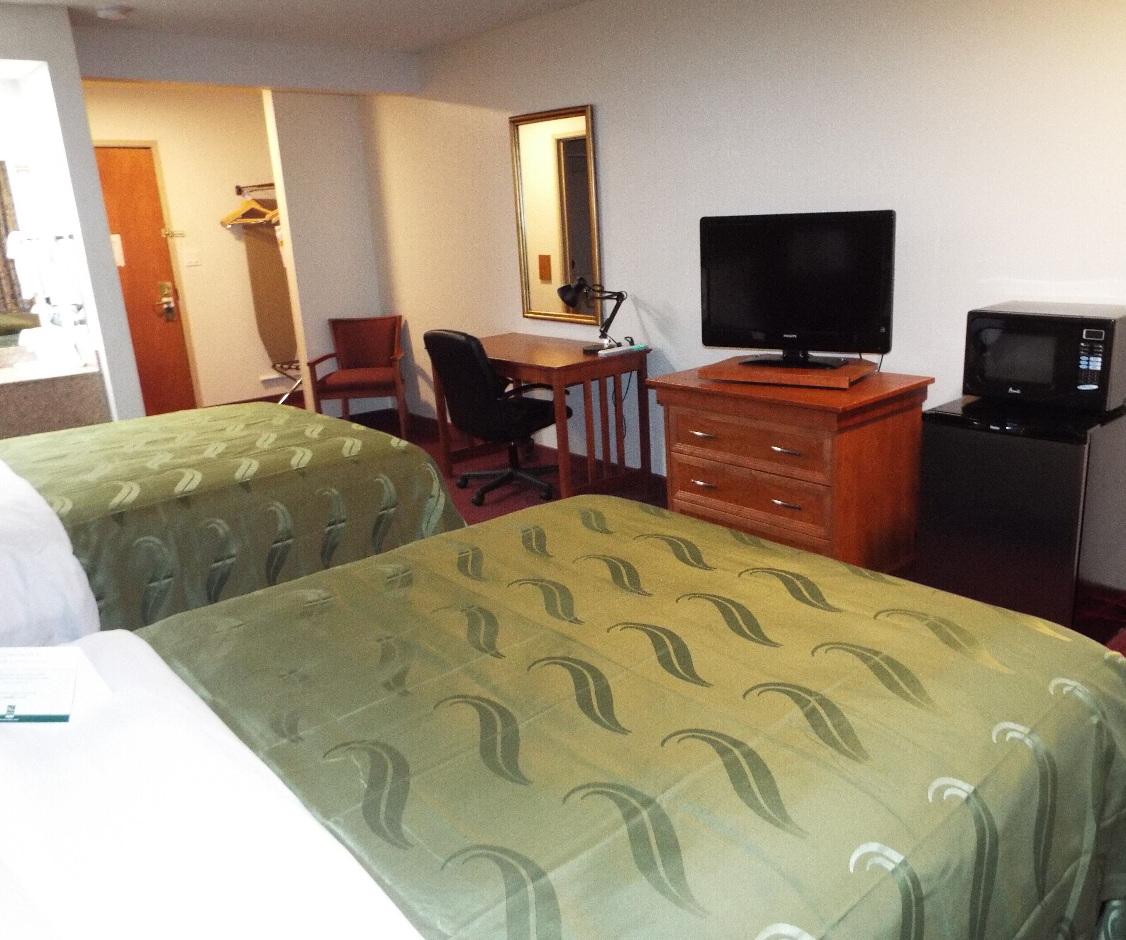 A hotel room with two beds, a desk with a chair, a television, and a microwave.