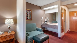 A hotel room with a green sofa, a small table with a lamp, a phone, a mirror, and a red carpeted floor.