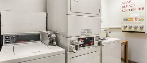 A laundry area with stacked washers and dryers, a wall-mounted soap and bleach dispenser, and a small table.