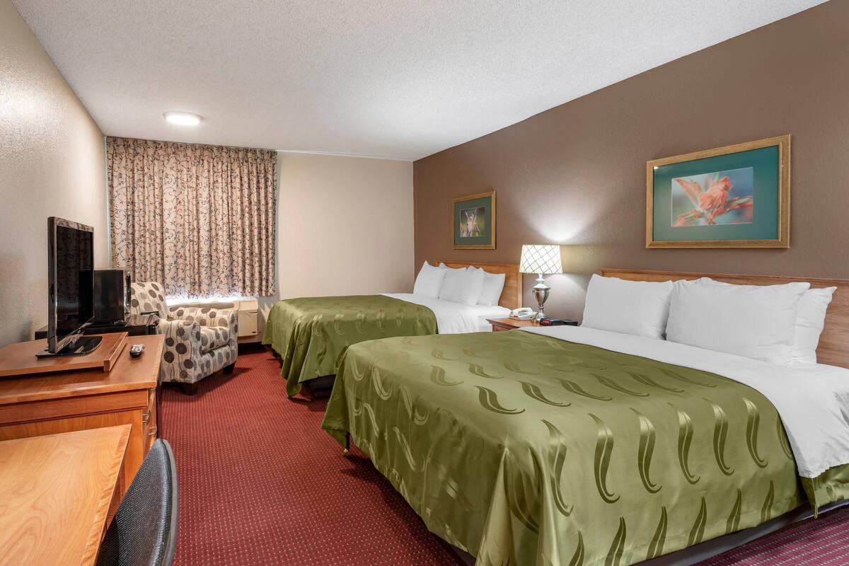 A hotel room with two beds, a desk with a TV, a chair, and a large window with curtains.