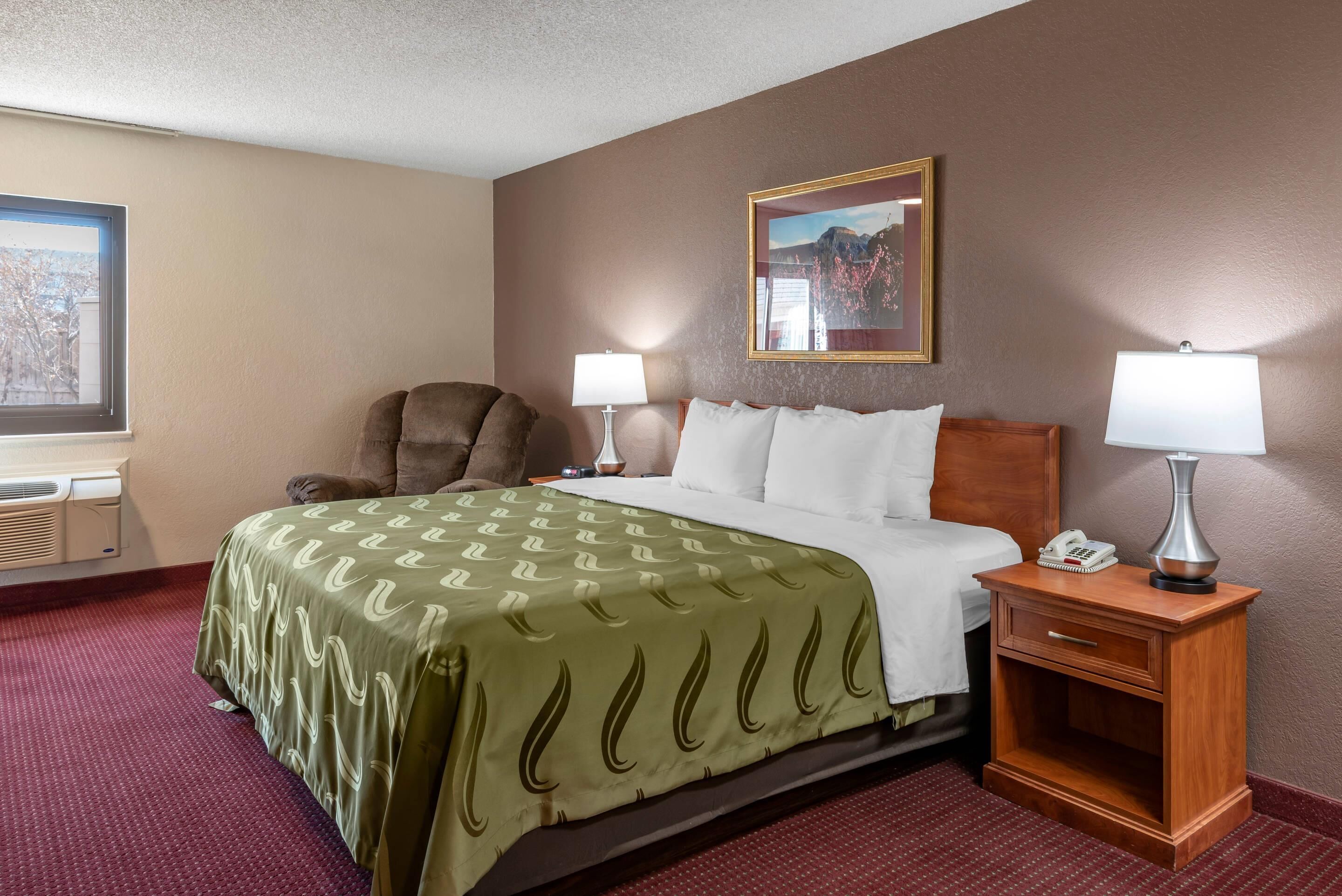 A hotel room with a bed, two bedside lamps, a chair, a nightstand, and a window.