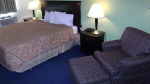 A hotel room with a bed, two bedside tables with lamps, a chair, and a small table. - Relax Inn (Davenport)
