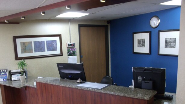 A reception desk with a computer, framed pictures on the wall, and a clock. - Relax Inn (Davenport)