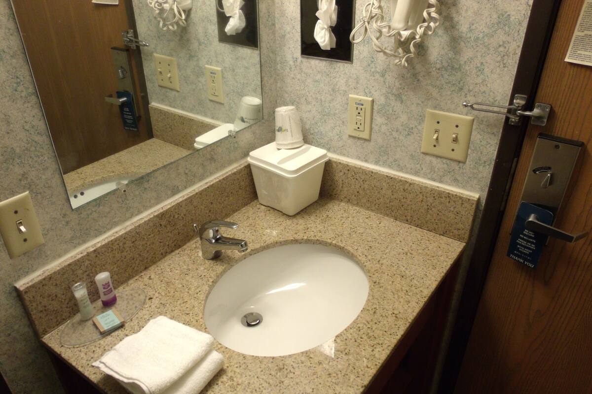 A bathroom with a granite countertop, a white sink, a mirror, a towel, and a toilet.