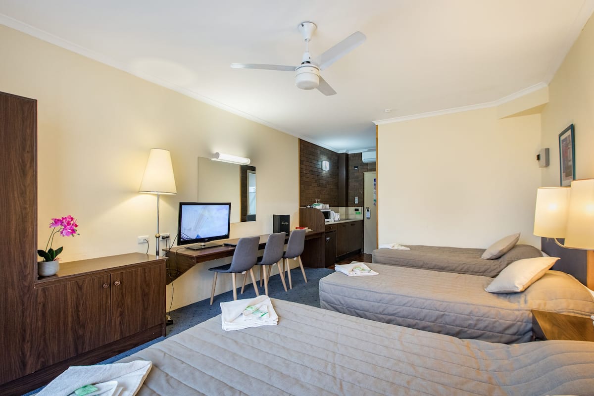 A hotel room with two beds, a desk with a computer, a TV, and a kitchenette.