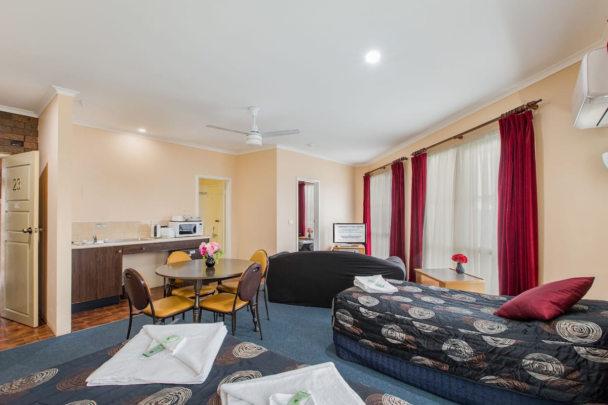 A hotel room with a bed, a sofa, a dining area, and a kitchen.