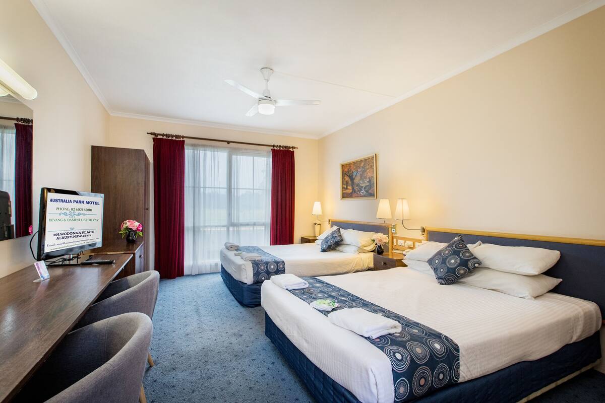 A hotel room with two beds, a desk, a chair, a desk lamp, and a ceiling fan.