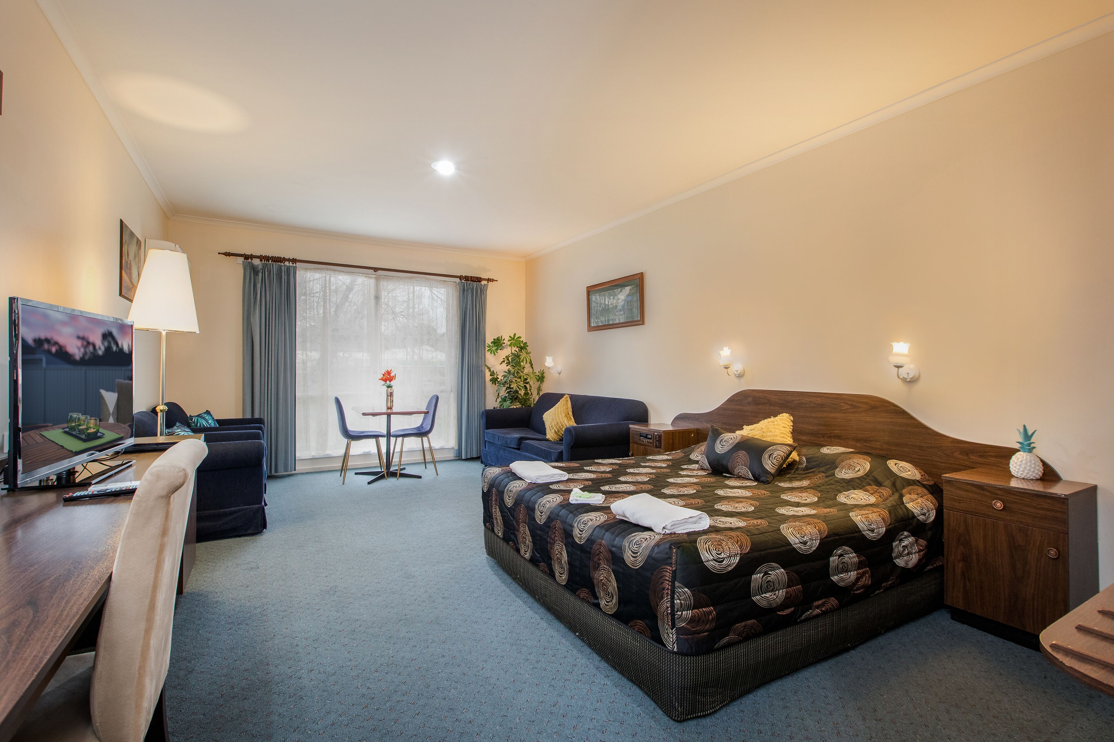 Una habitación de hotel con una cama, un escritorio, una silla, una mesita y un televisor.