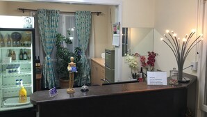 Zona de recepción de un hotel con un refrigerador lleno de bebidas, un maniquí de madera y un espejo que refleja la habitación.