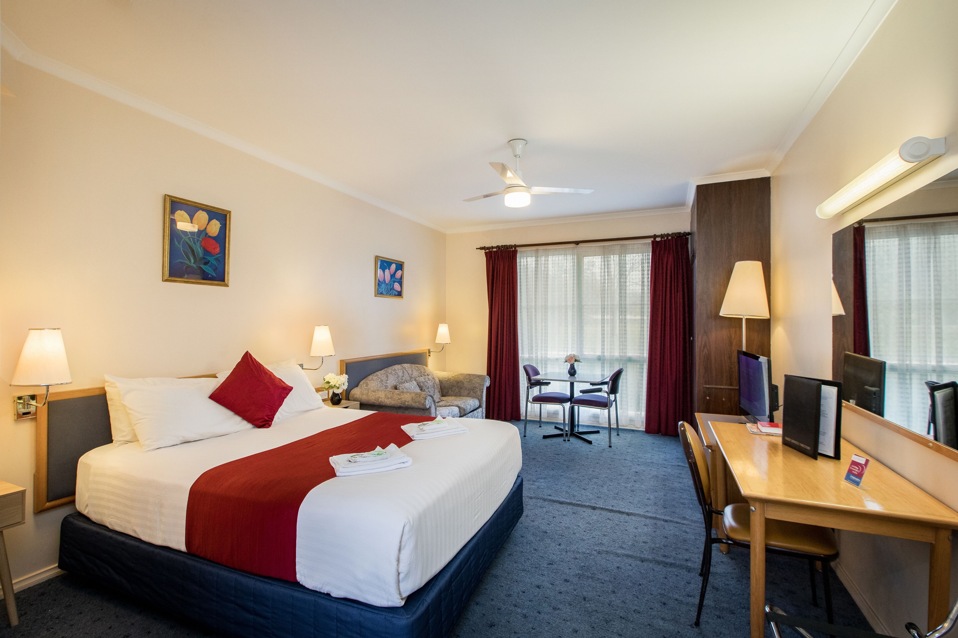 Habitación de hotel con cama, escritorio, sillas y televisor.