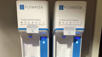 Dois dispensadores de água FLOWWATER com 7x Purificação Avançada, um lembrete para não descartar objetos que não sejam água no ralo, e um indicador luminoso azul.