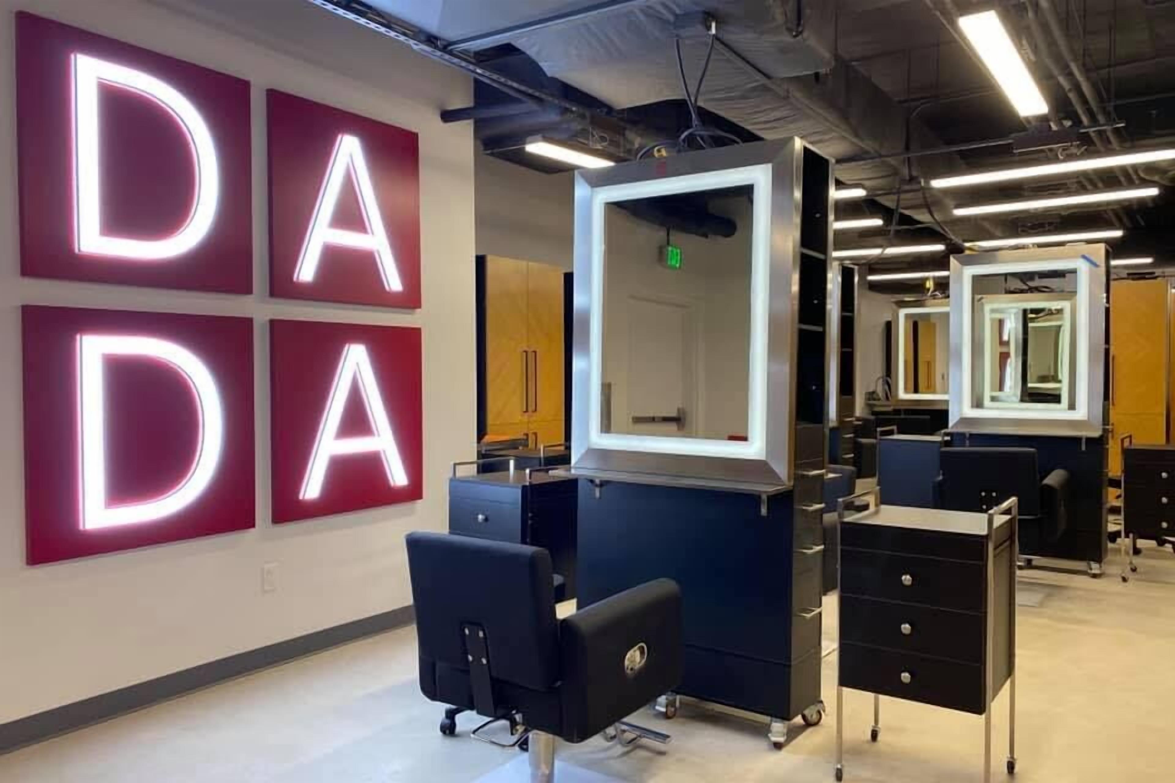 Un'elegante salone con insegne illuminate 'DADA', uno specchio centrale e diverse postazioni di lavoro.