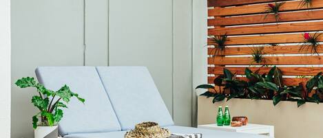 Un espace extérieur moderne aménagé avec des sièges, comprenant un fauteuil lounge bleu clair doté de coussins, une petite table avec une plante, et un mur végétalisé en bois où sont disposées différentes plantes.