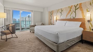 A hotel room with a large bed, a chair, a nightstand, and a view of the city.