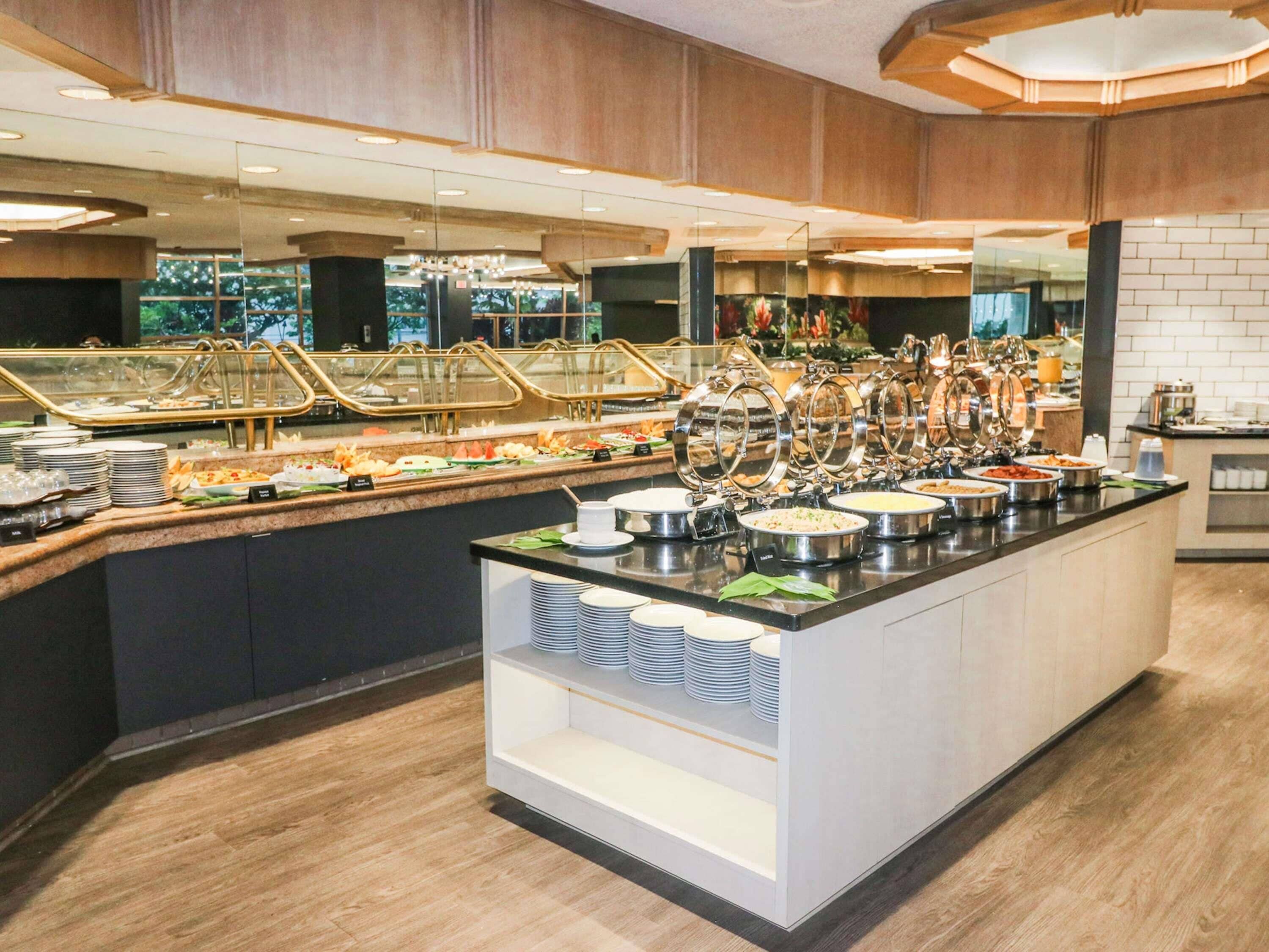 A buffet setup with multiple food stations, a glass display case, and a counter with stacked plates.