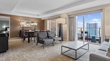 Habitación de hotel con comedor, sofá, mesa de centro y un amplio ventanal con vistas a la ciudad.