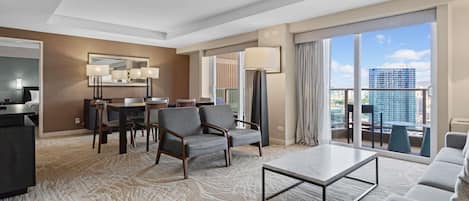 Une chambre d’hôtel comprenant un coin repas, un canapé, une table basse et une grande fenêtre donnant sur la ville.