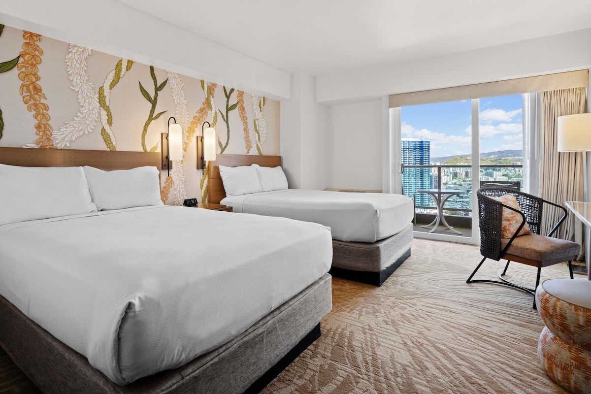 Habitación de hotel con dos camas, un ventanal con vistas a la ciudad, un balcón con una silla y un detalle decorativo en la pared.