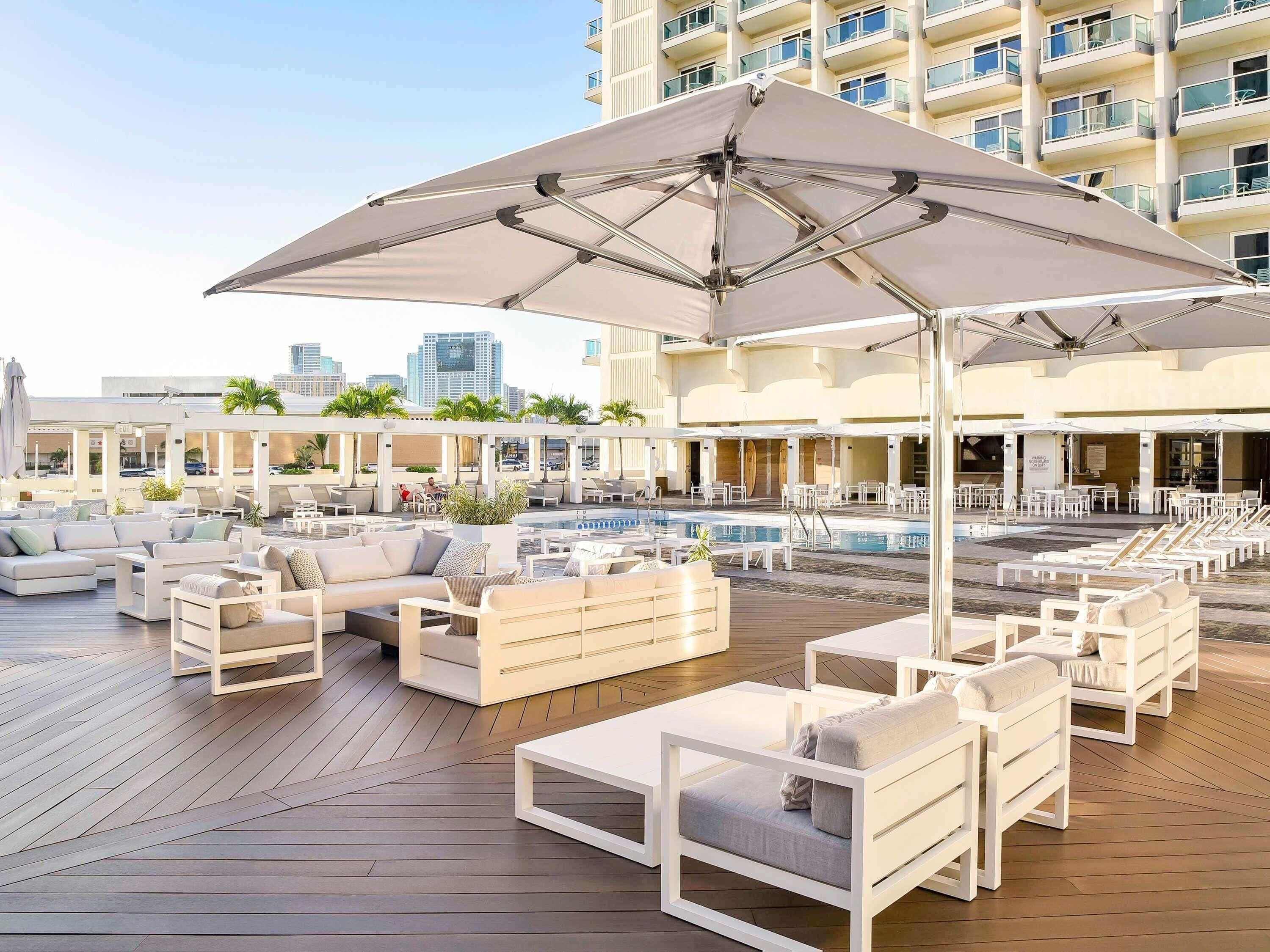 A rooftop pool area with lounge chairs, a pool, and a view of a city skyline.