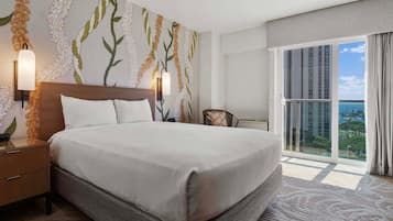 A hotel room with a large bed, a nightstand, a wall-mounted lamp, a chair, and a view of the city through a large window.