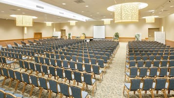 Ein Konferenzraum mit Reihen von Stühlen, einer Projektionsleinwand und einer großen Pflanze.