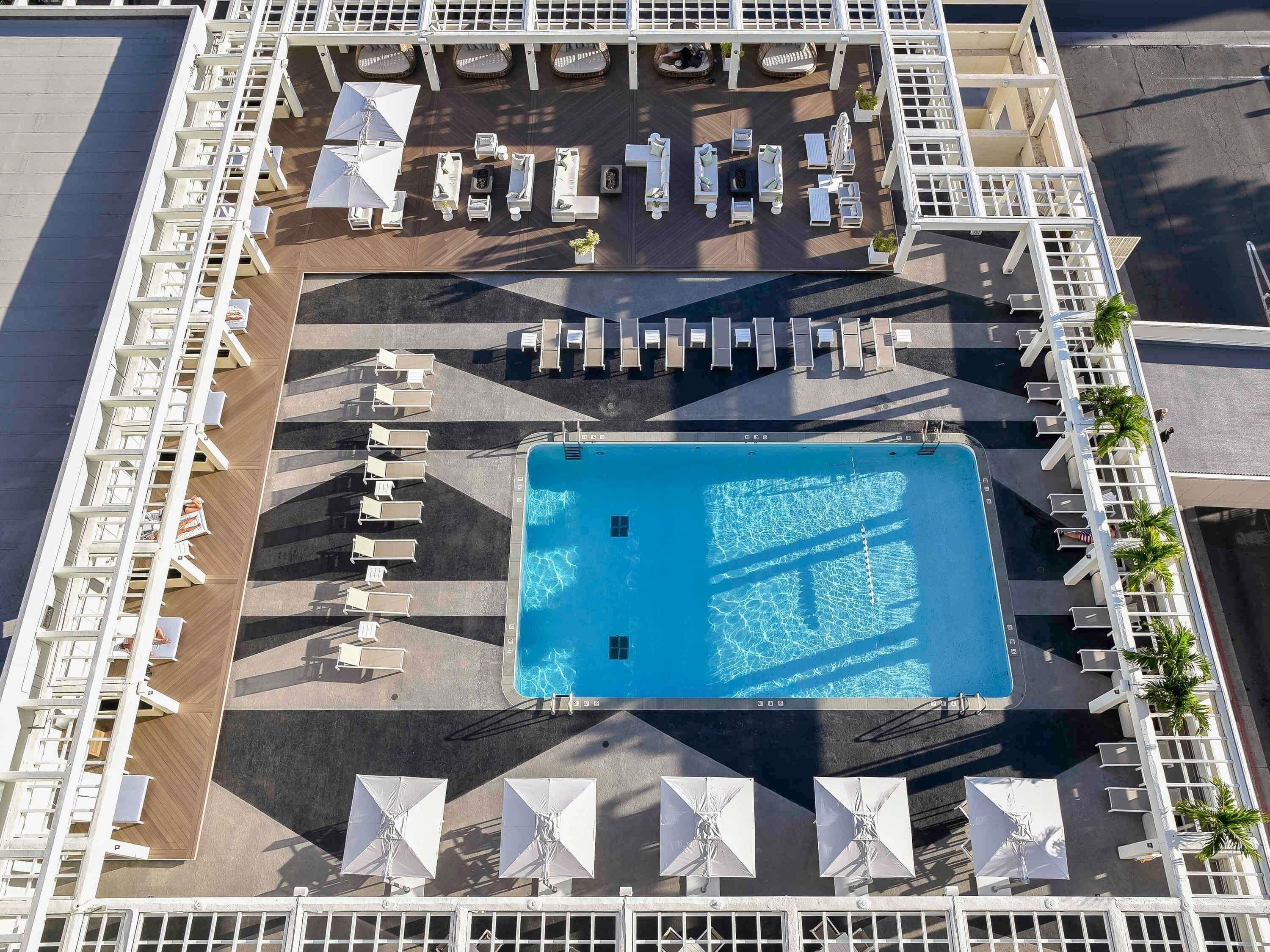 Vista aérea de un hotel con una piscina central, múltiples zonas de descanso con sillas y sombrillas, y una distribución ordenada de asientos al aire libre.