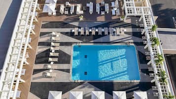Vista aérea de un hotel con una piscina central, múltiples zonas de descanso con sillas y sombrillas, y una distribución ordenada de asientos al aire libre.