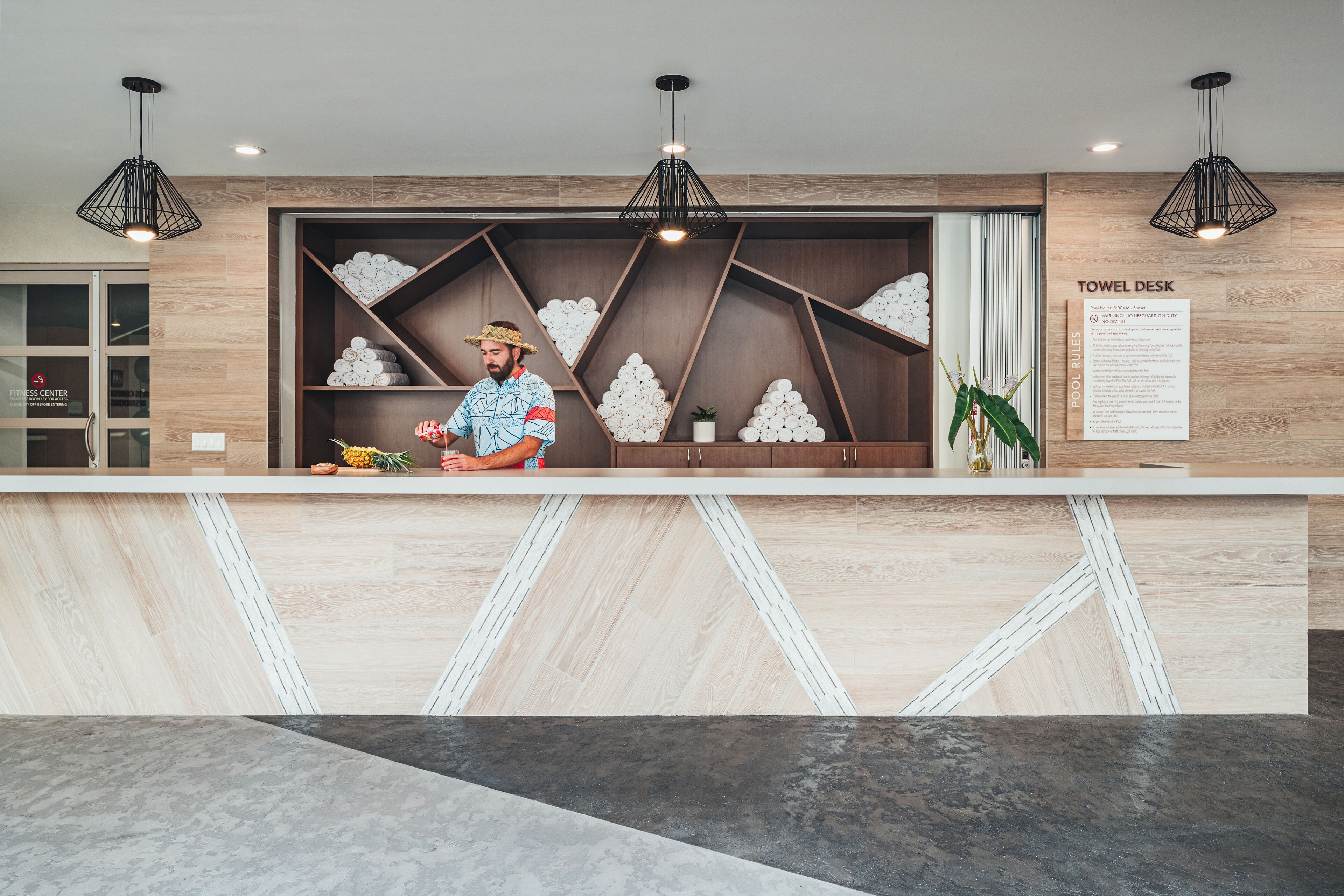 A reception desk with a towel rack, a sign indicating towel policies, and a wooden wall with geometric patterns.