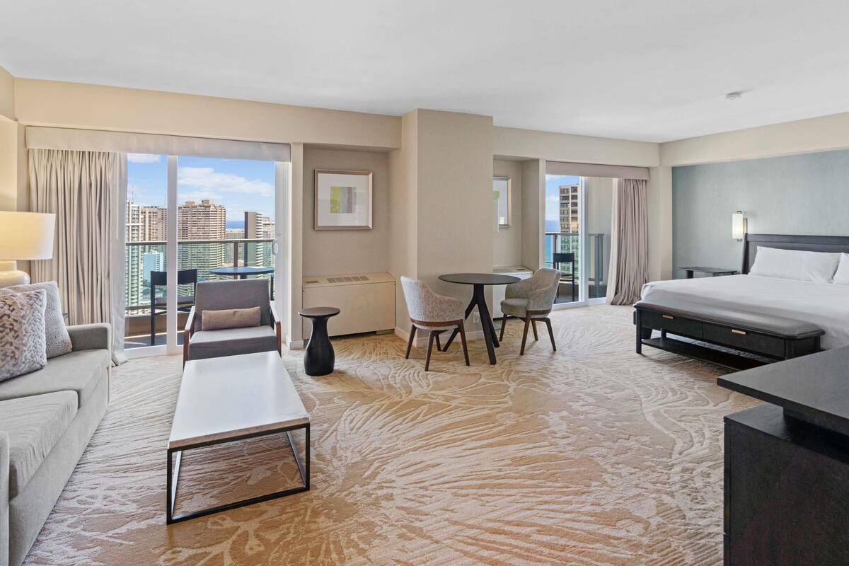 Habitación de hotel con cama, escritorio, sofá, silla, una mesita y vistas a la ciudad.