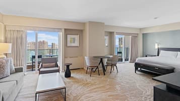 A hotel room with a bed, a desk, a sofa, a chair, a small table, and a view of the city.