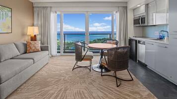 A modern hotel room with a balcony, a dining area, a sofa, and a kitchen.