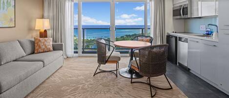 A modern hotel room with a balcony, a dining area, a sofa, and a kitchen.