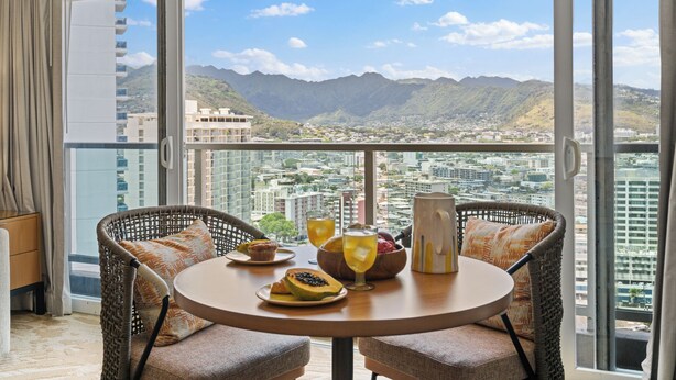 Un balcón con sillones de mimbre, una mesa con productos para el desayuno y vistas de la ciudad.
