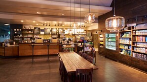 Un café acogedor con barra de madera, zona de estar y estantes llenos de aperitivos y bebidas.