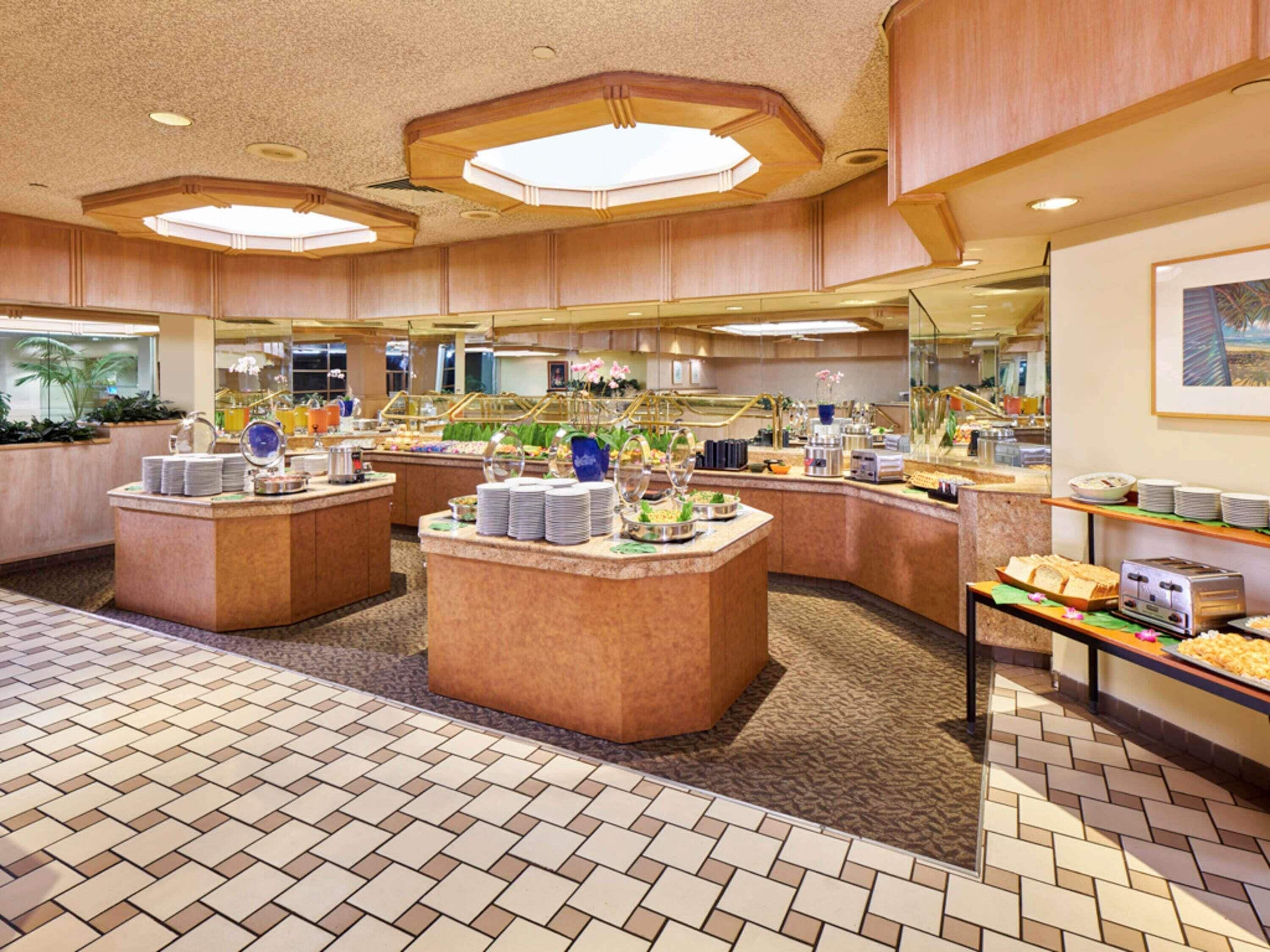 Un área de desayuno de hotel con varias estaciones de buffet, piso de baldosas y un ventanal con vistas.