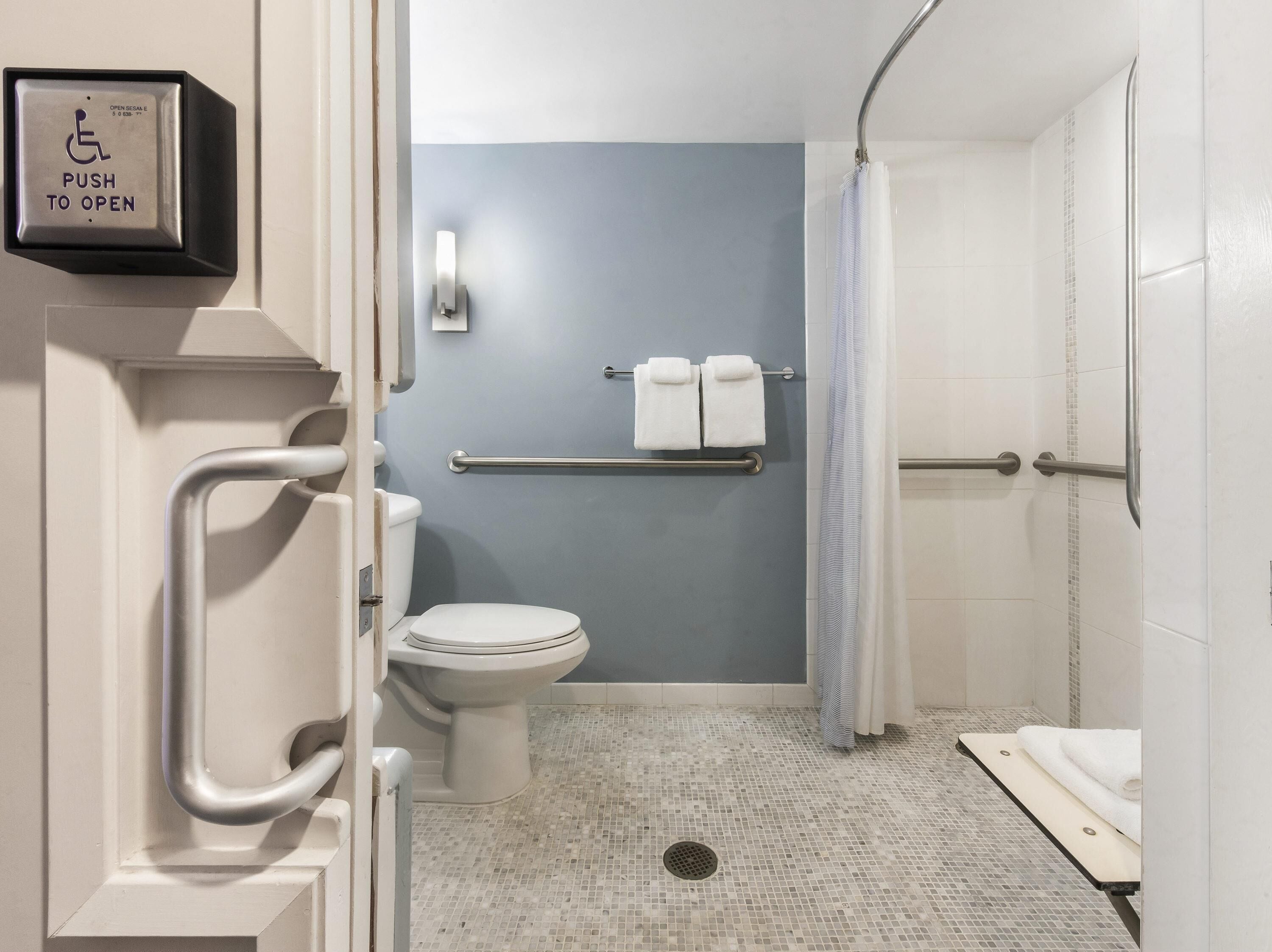 Un baño con inodoro, barra de apoyo y zona de ducha.