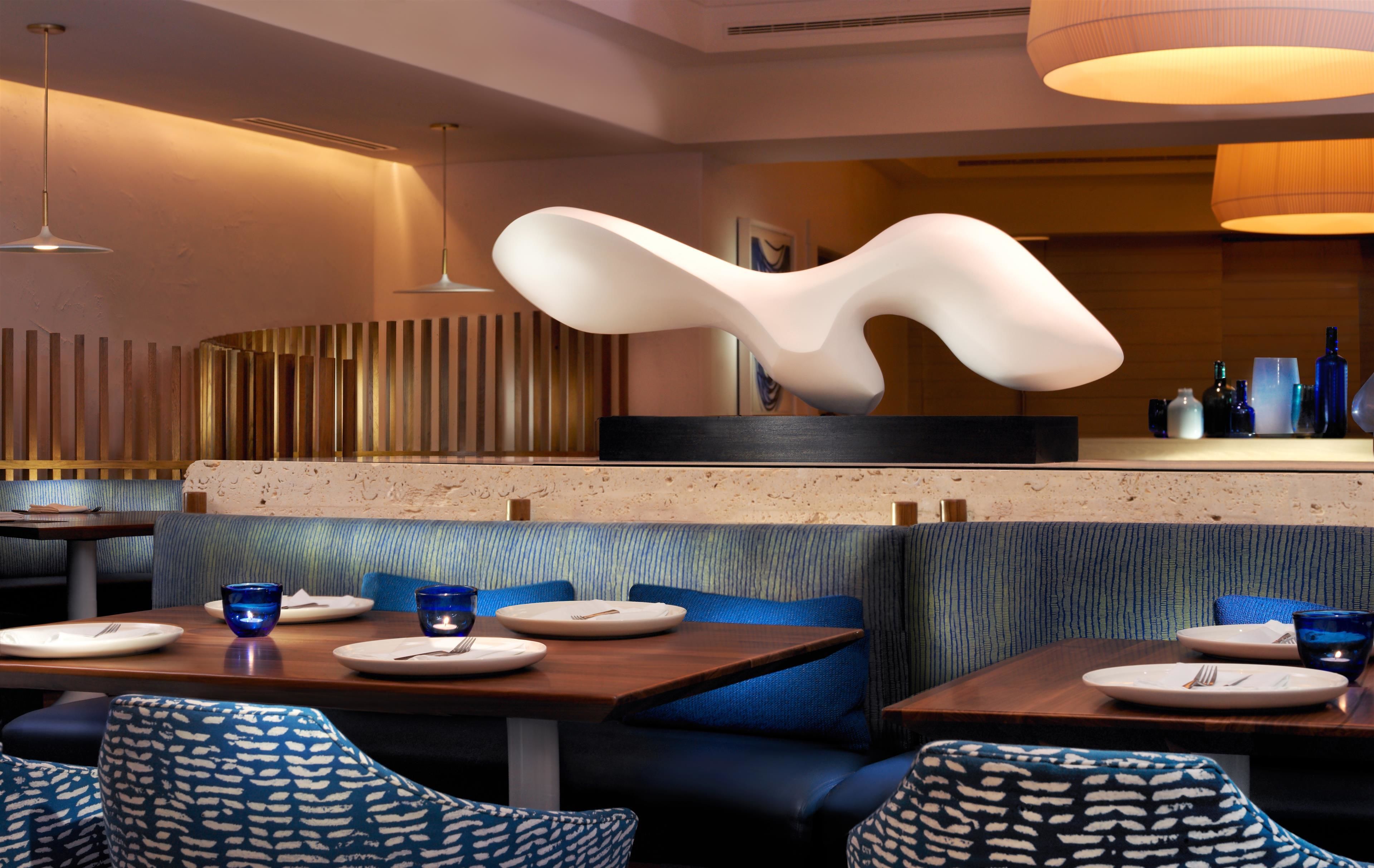 Ein modernes Restaurant mit blau gepolsterten Sitzbänken, Holztischen und zeitgemäßen Leuchten.