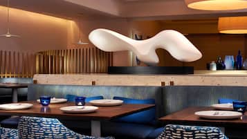 Ein modernes Restaurant mit blau gepolsterten Sitzbänken, Holztischen und zeitgemäßen Leuchten.
