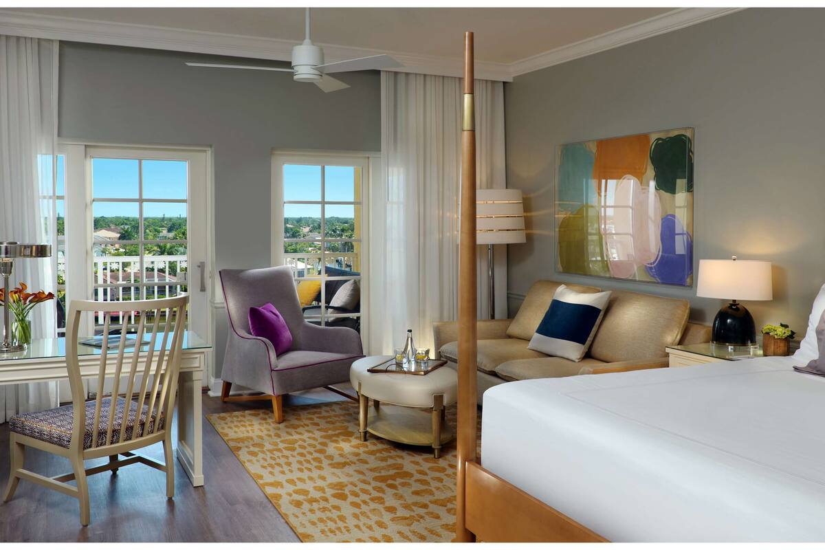 Une chambre d’hôtel avec un grand lit, un canapé, un fauteuil, une petite table et un balcon avec vue.