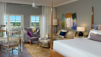A hotel room with a large bed, a sofa, a chair, a small table, and a balcony with a view.