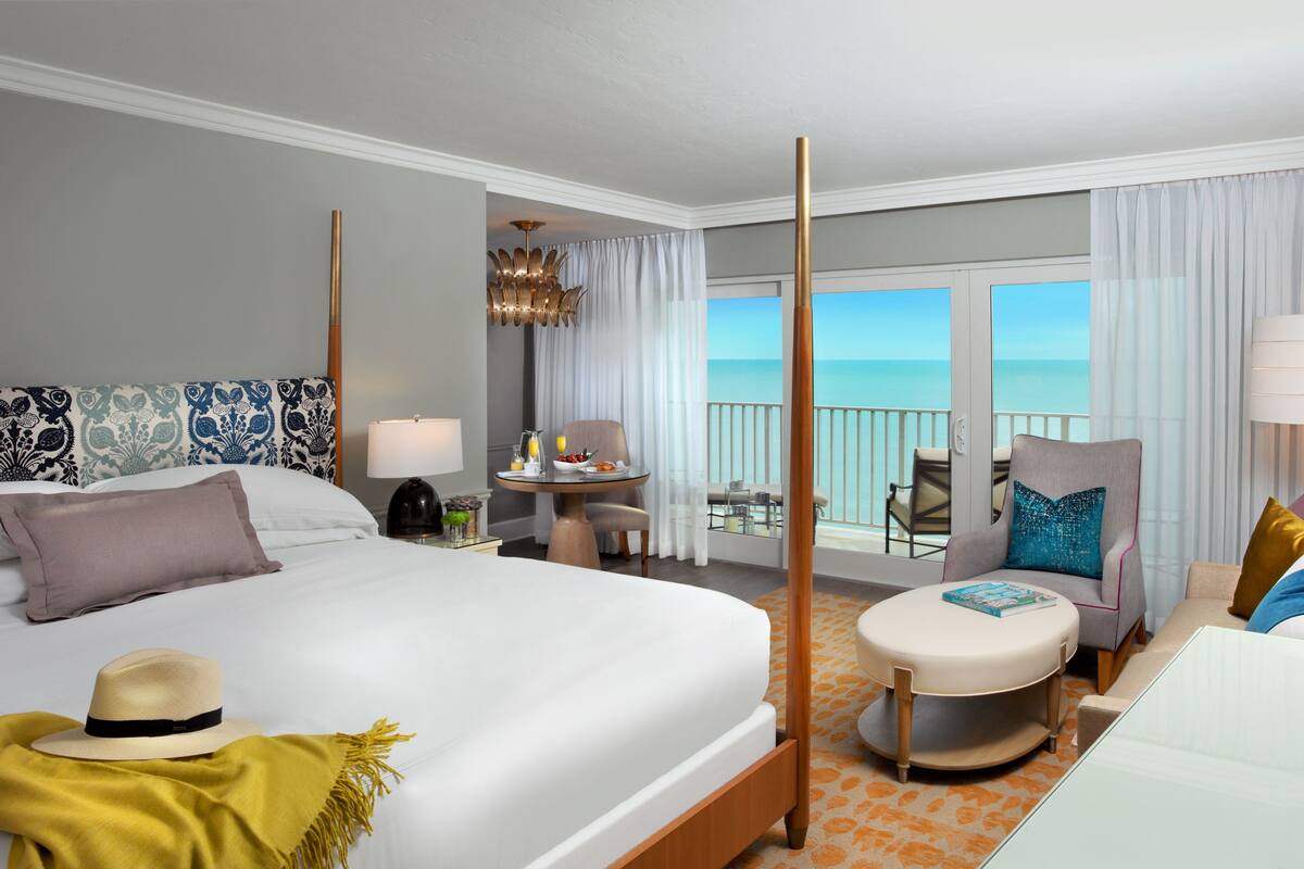 Une chambre d’hôtel avec un grand lit, un balcon avec vue, une petite table avec une lampe et une chaise.