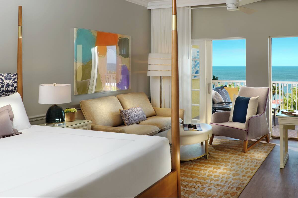 Une chambre d’hôtel comprenant un lit, un canapé, une chaise, une table et un balcon avec vue sur la mer.