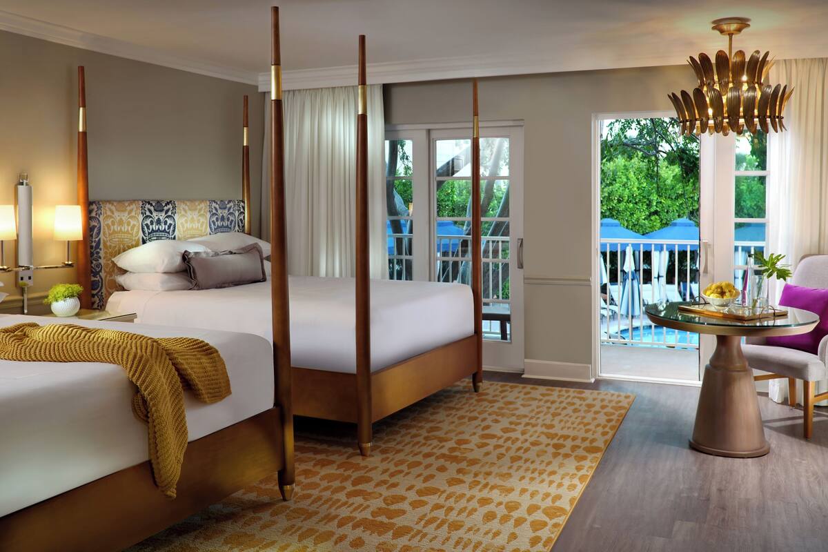 Une chambre d’hôtel avec un grand lit, une petite table sur laquelle est posé un vase, une chaise et une vue sur l’extérieur.