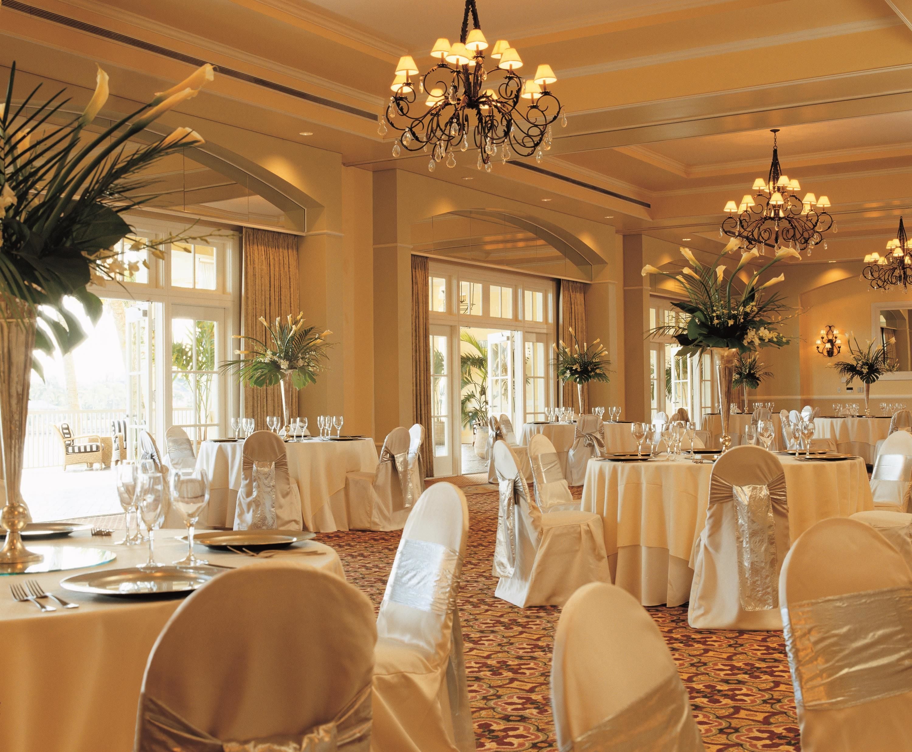 A banquet hall with round tables, white tablecloths, and chairs with white covers.