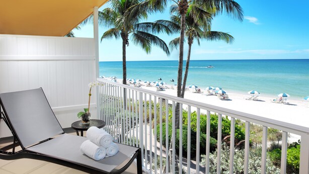 Un balcón con vista a la playa, barandillas blancas y una silla de lounge con toallas.